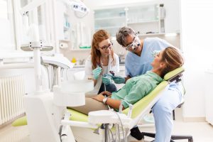 Medical dentist team in dental office talking with female patient and preparing for treatment.